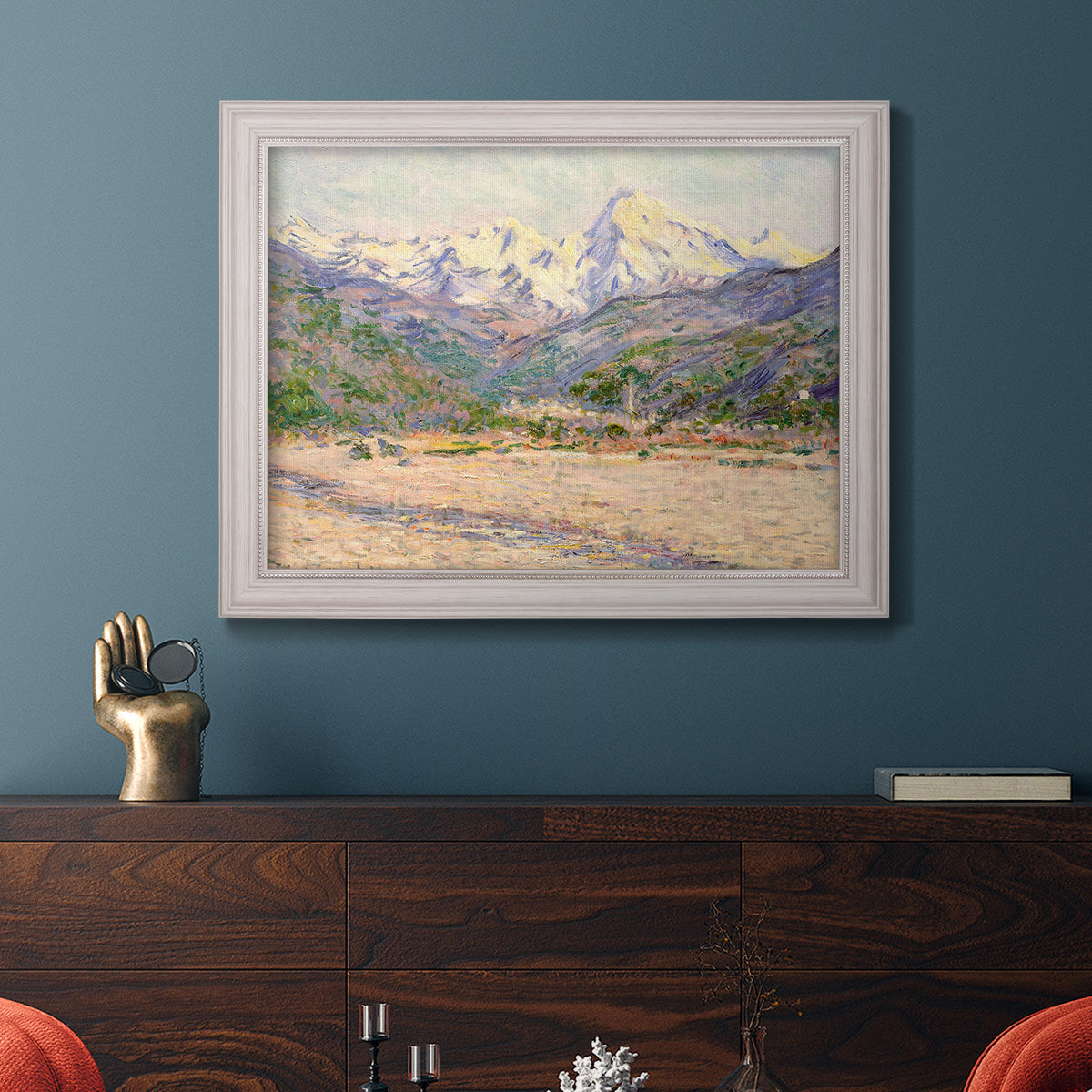 Impressionist valley landscape in southern France by Claude Monet in an ornate weathered white frame displayed in a dark-toned interior setting.