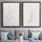 Set of two walnut barnwood framed canvas prints depicting paired minimalist botanical line drawings with thin gray contours, sparse stems, and clean white fields above a sofa in a contemporary living room.