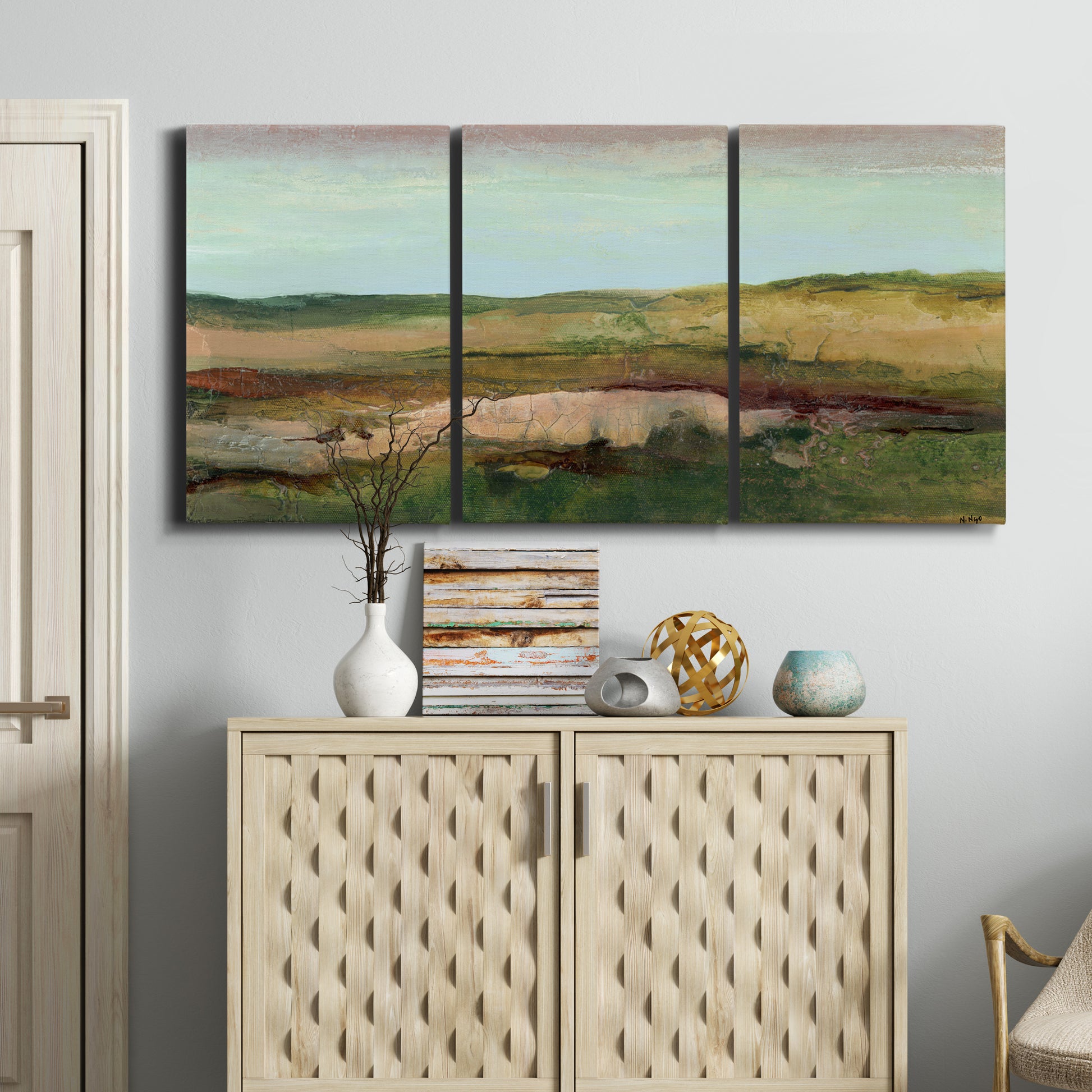 Three-panel canvas wall art featuring pastoral landscape with winding road, displayed above a cabinet in an entryway.