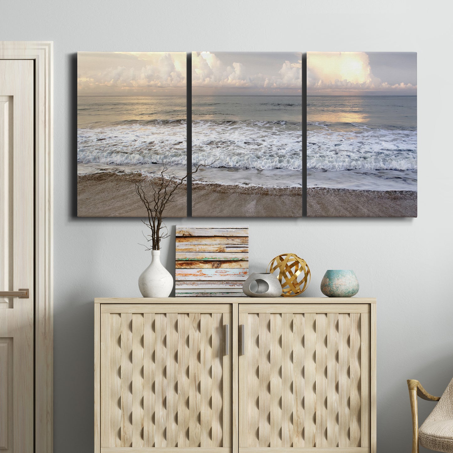 Three-panel canvas wall art featuring calm coastal shoreline seascape, displayed above a cabinet in an entryway.