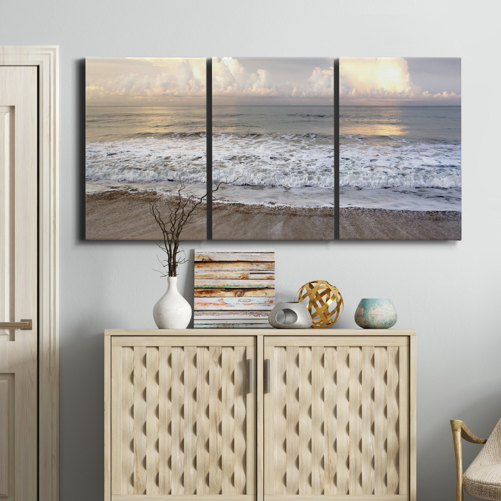 Three-panel canvas wall art featuring calm coastal shoreline seascape, displayed above a cabinet in an entryway.