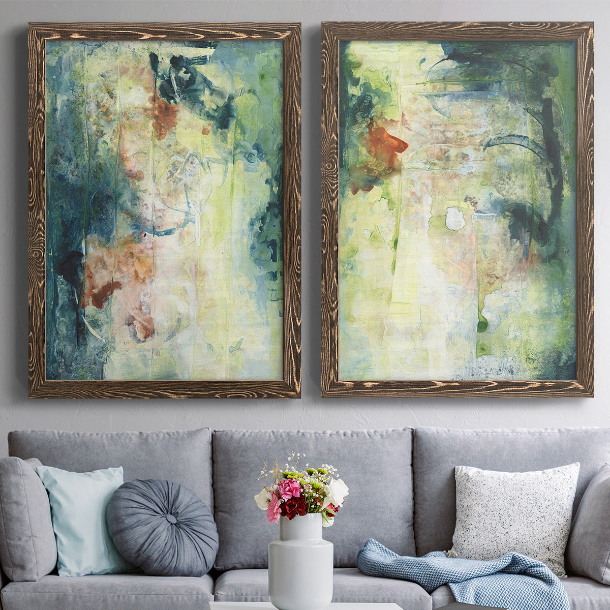Set of two walnut barnwood framed canvas prints depicting paired nature-inspired mixed-media abstracts with vertical organic marks, pale light passages, and weathered surfaces above a sofa in a contemporary living room.