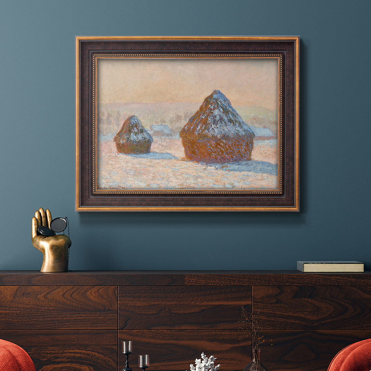 Impressionist winter haystack scene by Claude Monet in an ornate bronzed mahogany wood frame displayed in a dark-toned interior setting.
