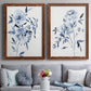 Set of two maple barnwood framed canvas prints depicting paired expressive watercolor botanical paintings with indigo blossoms, gestural blue leaves, and airy white space above a sofa in a contemporary living room.