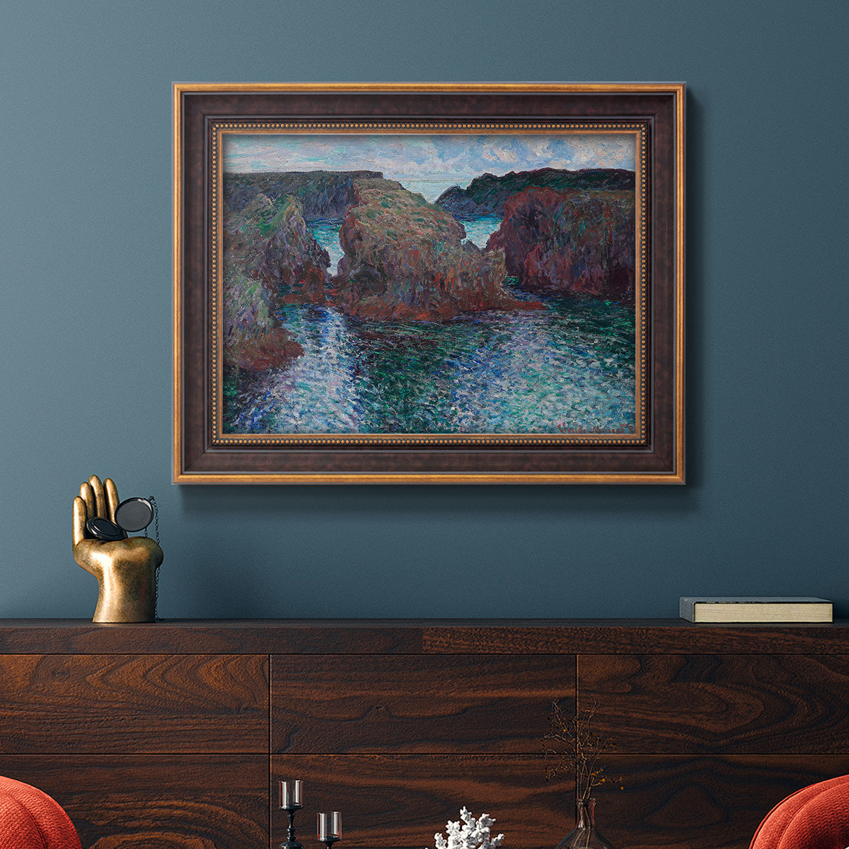 Impressionist rocky seascape by Claude Monet in an ornate bronzed mahogany wood frame displayed in a dark-toned interior setting.