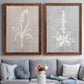 Set of two maple barnwood framed canvas prints depicting paired rustic minimalist botanical prints with delicate stems, leaves, and blossoms against gray taupe and pale blue panels above a sofa in a contemporary living room.