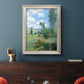 Impressionist pastoral landscape with poppy fields by Claude Monet in an ornate champagne frame displayed in a dark-toned interior setting.