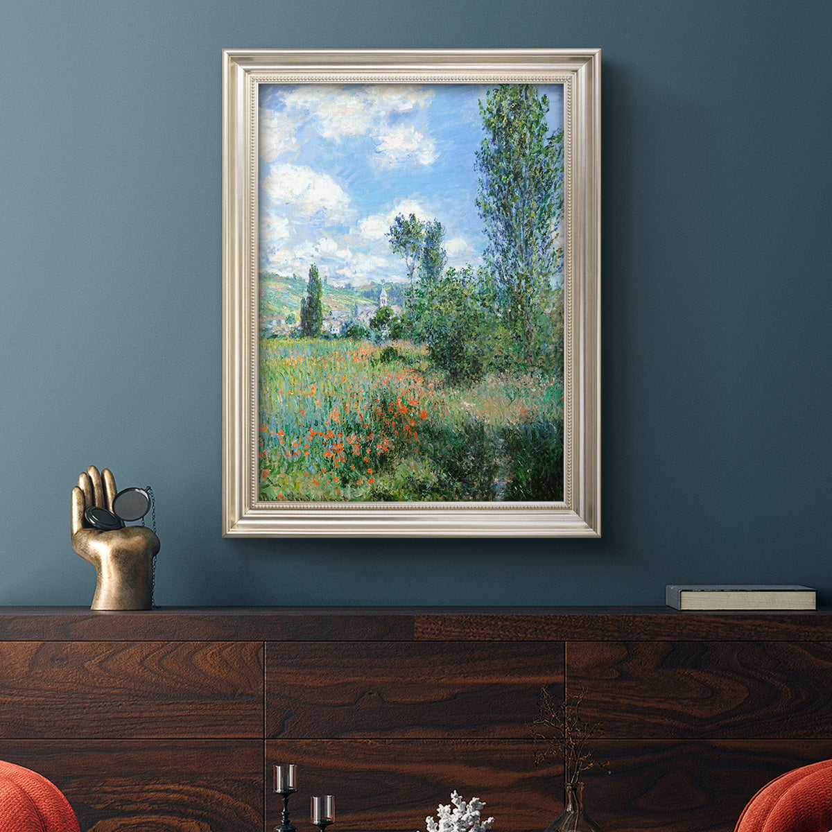 Impressionist pastoral landscape with poppy fields by Claude Monet in an ornate champagne frame displayed in a dark-toned interior setting.