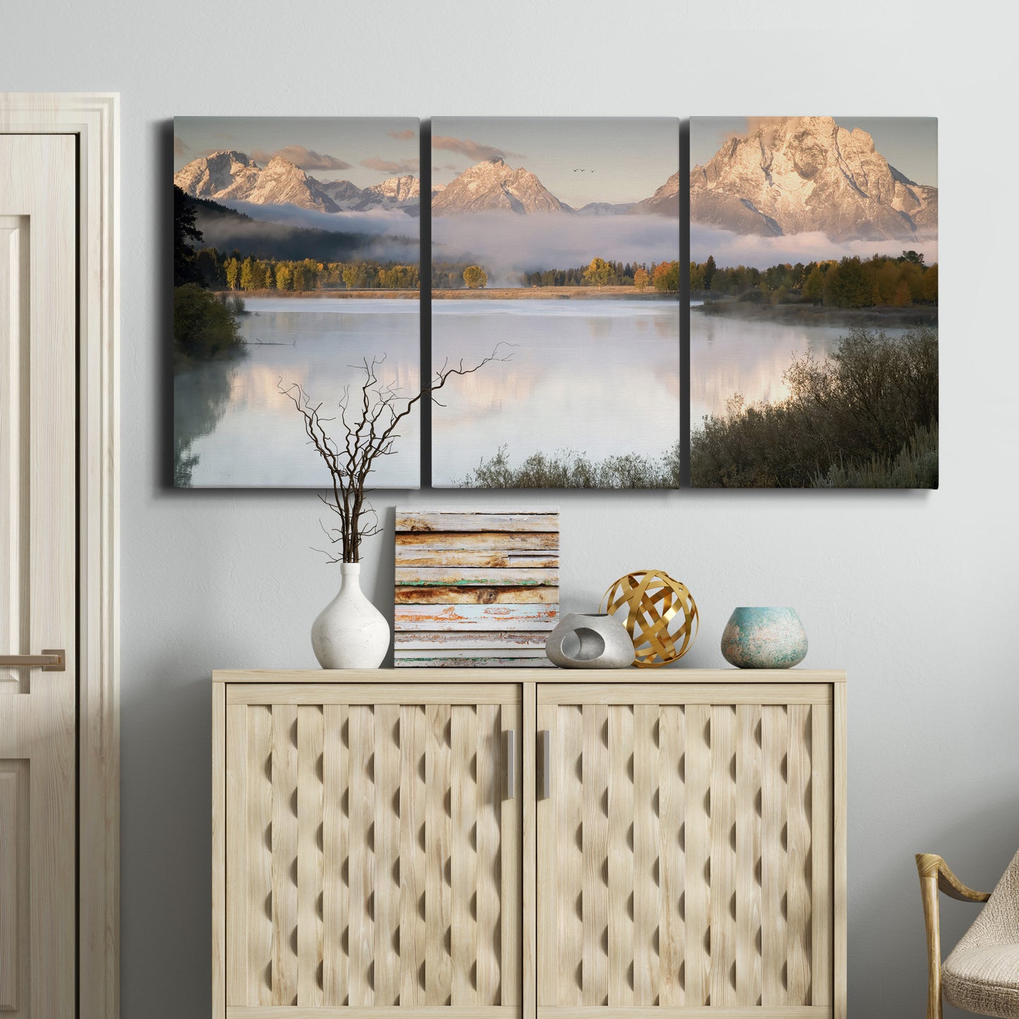 Three-panel canvas wall art featuring fog drifting over winding river, displayed above a cabinet in an entryway.