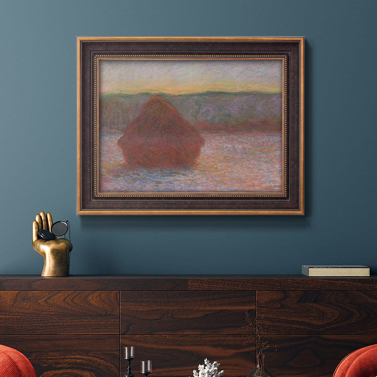 Impressionist haystack sunset scene in winter by Claude Monet in an ornate bronzed mahogany wood frame displayed in a dark-toned interior setting.