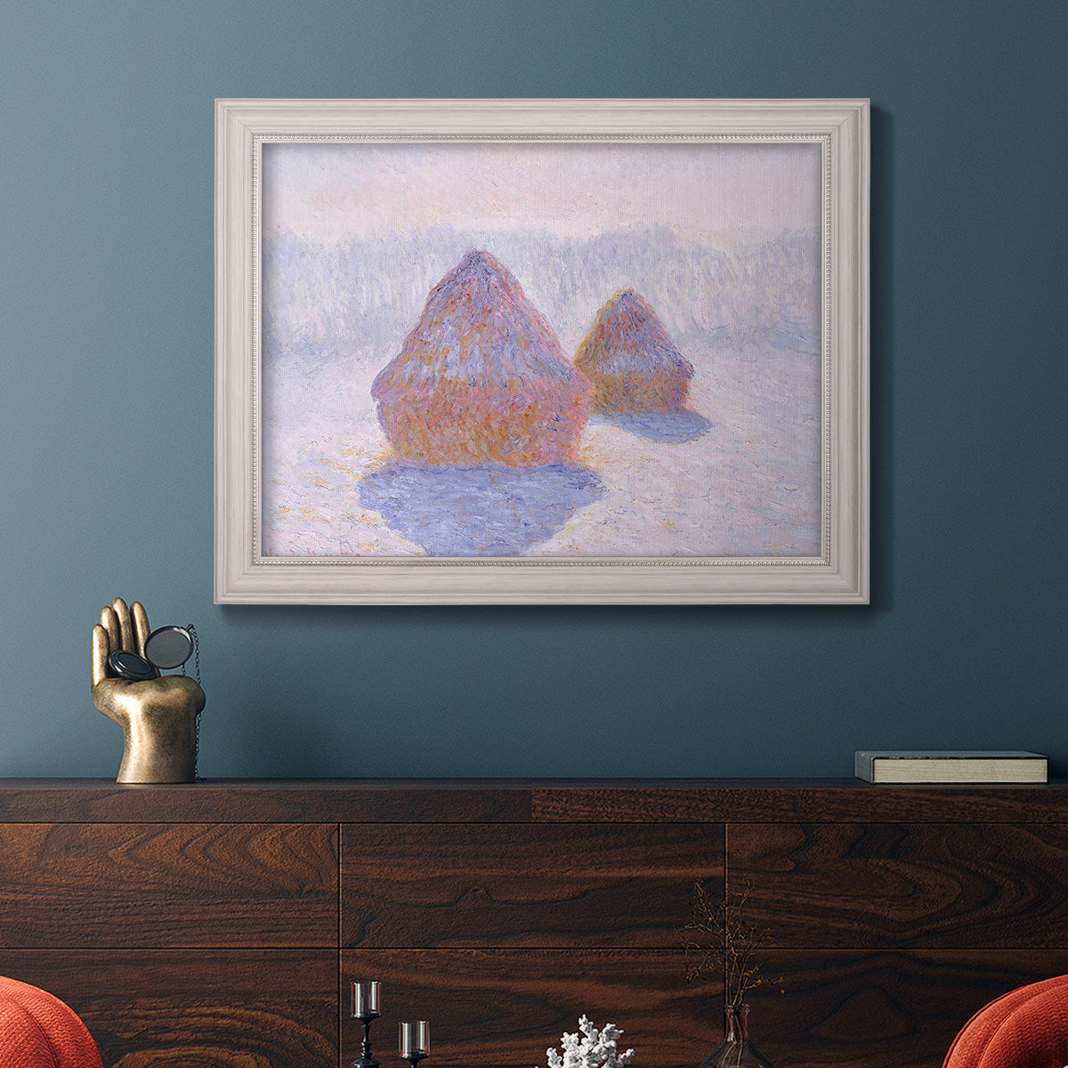 Impressionist winter haystack scene with sunlight by Claude Monet in an ornate weathered white frame displayed in a dark-toned interior setting.
