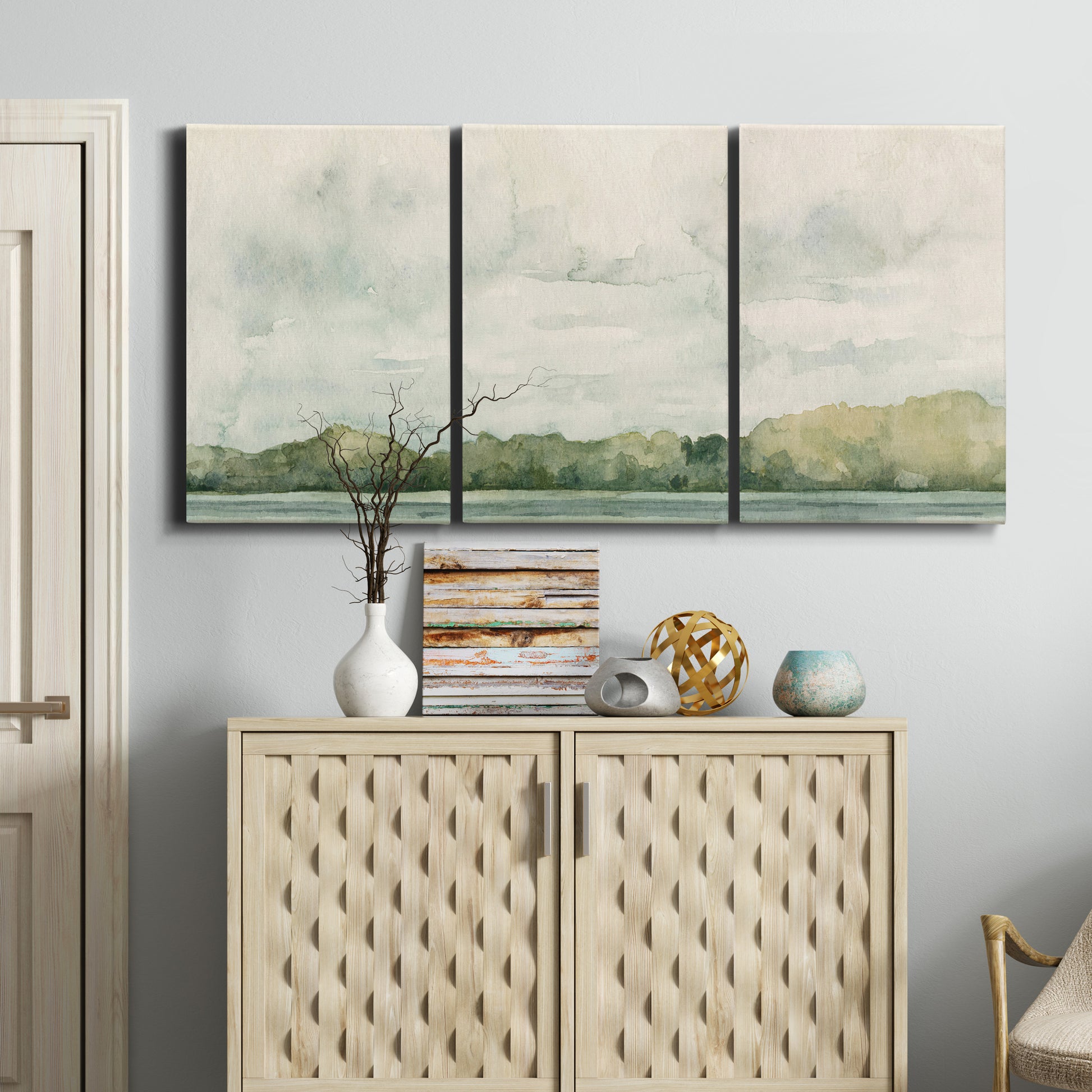 Three-panel canvas wall art featuring riverbank landscape with trees, displayed above a cabinet in an entryway.