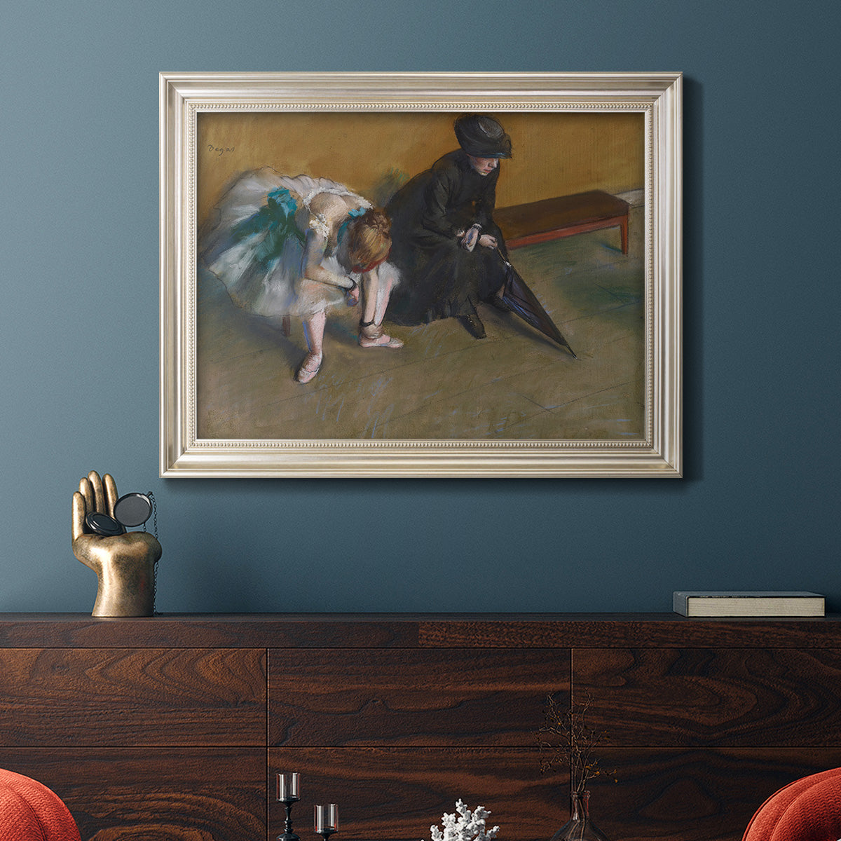 Impressionist portrait of a seated woman by Edgar Degas in an ornate champagne frame displayed in a dark-toned interior setting.