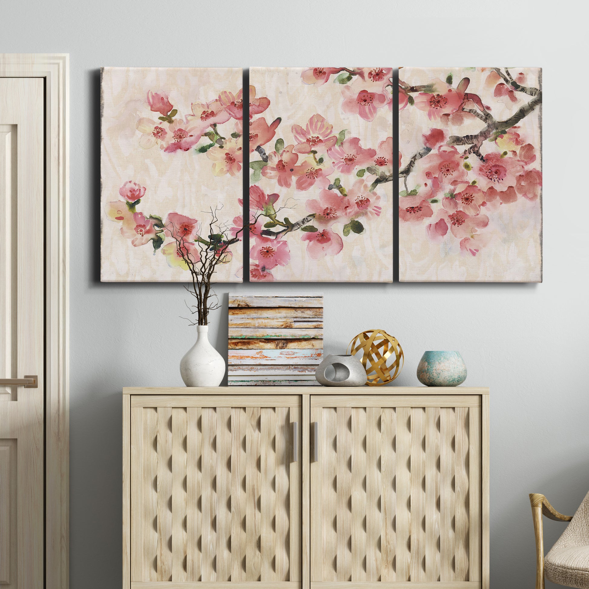 Three-panel canvas wall art featuring blooming cherry blossom branches, displayed above a cabinet in an entryway.