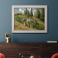 Impressionist countryside harvest scene by Camille Pissarro in an ornate weathered white frame displayed in a dark-toned interior setting.