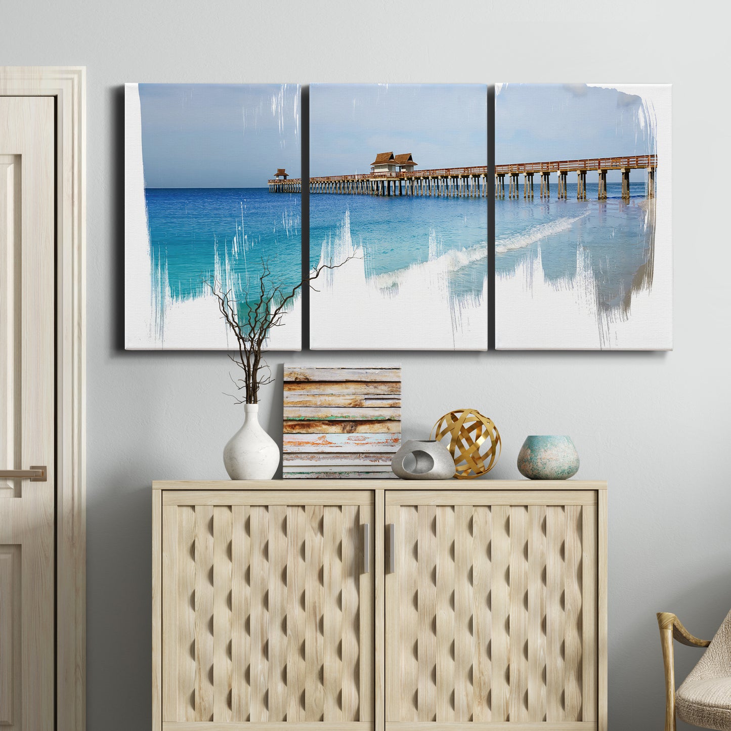 Three-panel canvas wall art featuring coastal pier extending over water, displayed above a cabinet in an entryway.