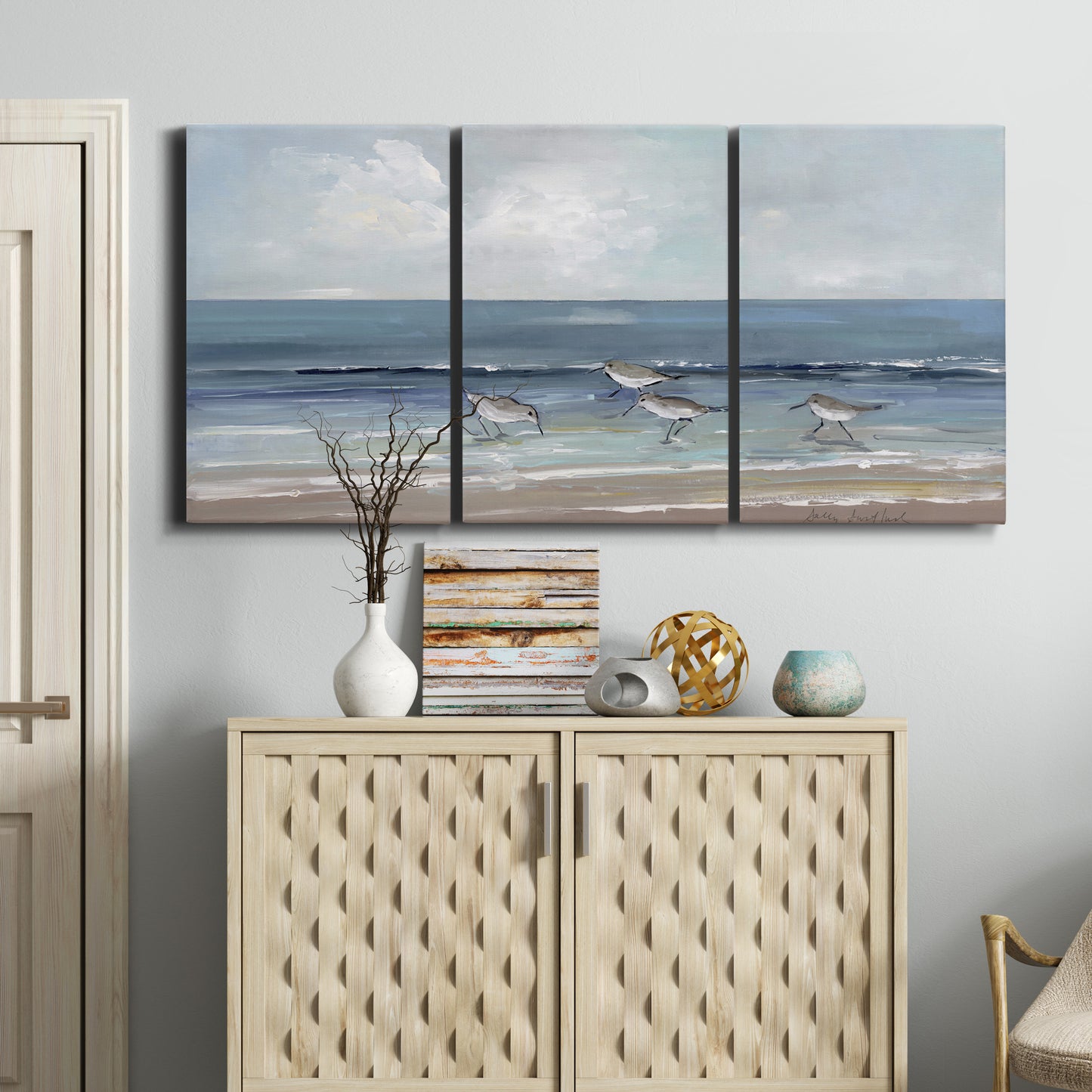 Three-panel canvas wall art featuring shore birds searching along beach, displayed above a cabinet in an entryway.
