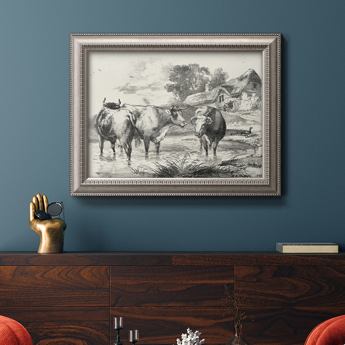 Classical rural landscape artwork by Nicolas Berchem in an ornate vintage silver frame displayed in a dark-toned interior setting.