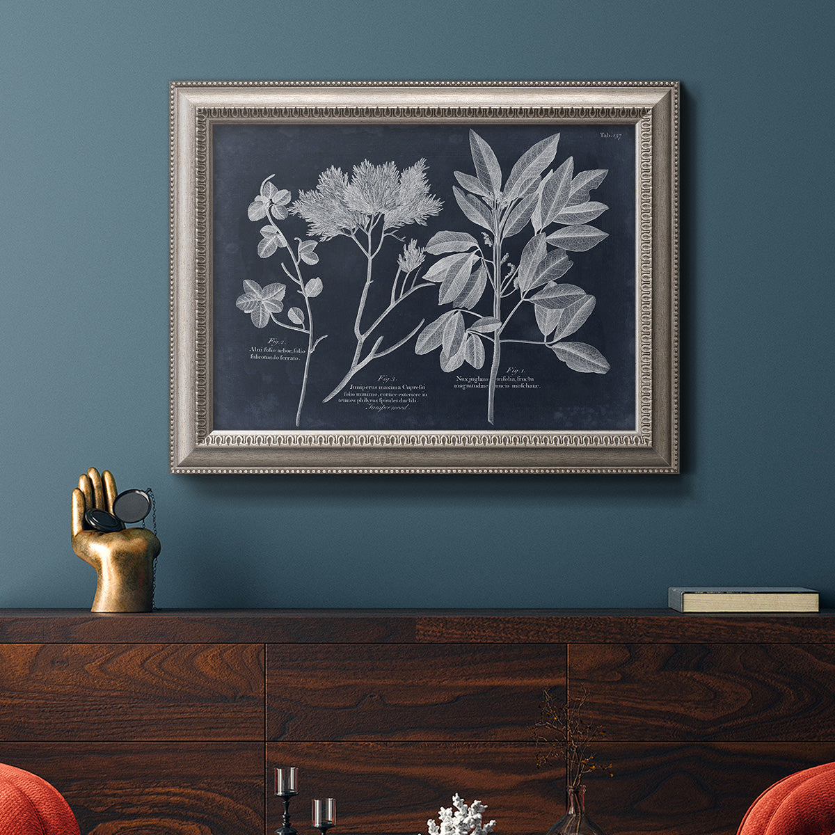 Vintage botanical leaf illustration on dark background in an ornate vintage silver frame displayed in a dark-toned interior setting.