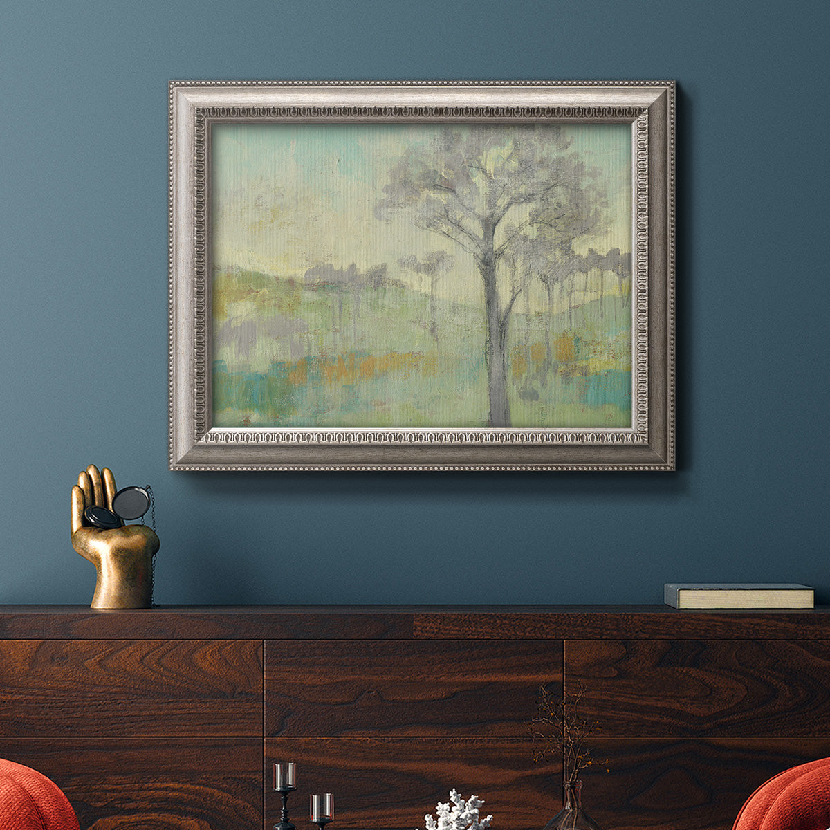 Classical watercolor landscape with trees in an ornate vintage silver frame displayed in a dark-toned interior setting.