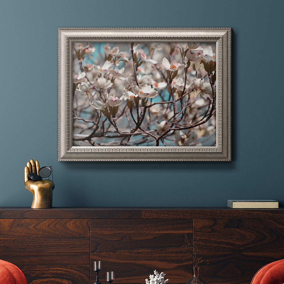 Contemporary dogwood blossom floral photography in an ornate vintage silver frame displayed in a dark-toned interior setting.
