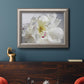 Soft white peony close-up in an ornate vintage silver frame displayed in a dark-toned interior setting.
