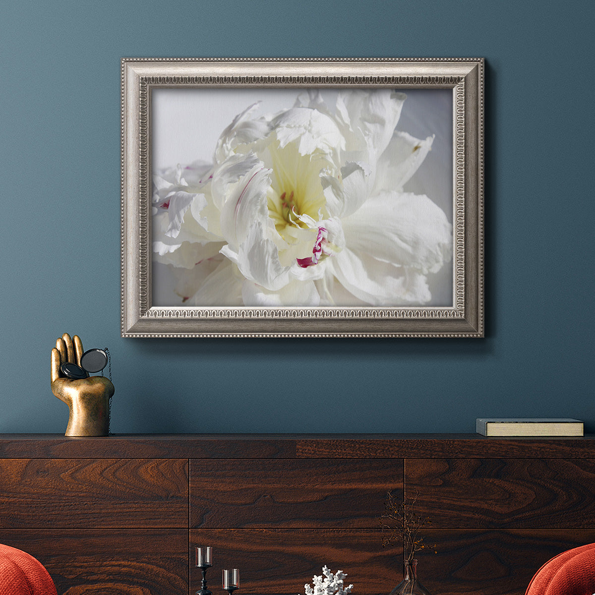 Soft white peony close-up in an ornate vintage silver frame displayed in a dark-toned interior setting.
