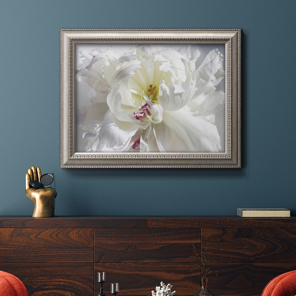 White floral photography close-up in an ornate vintage silver frame displayed in a dark-toned interior setting.
