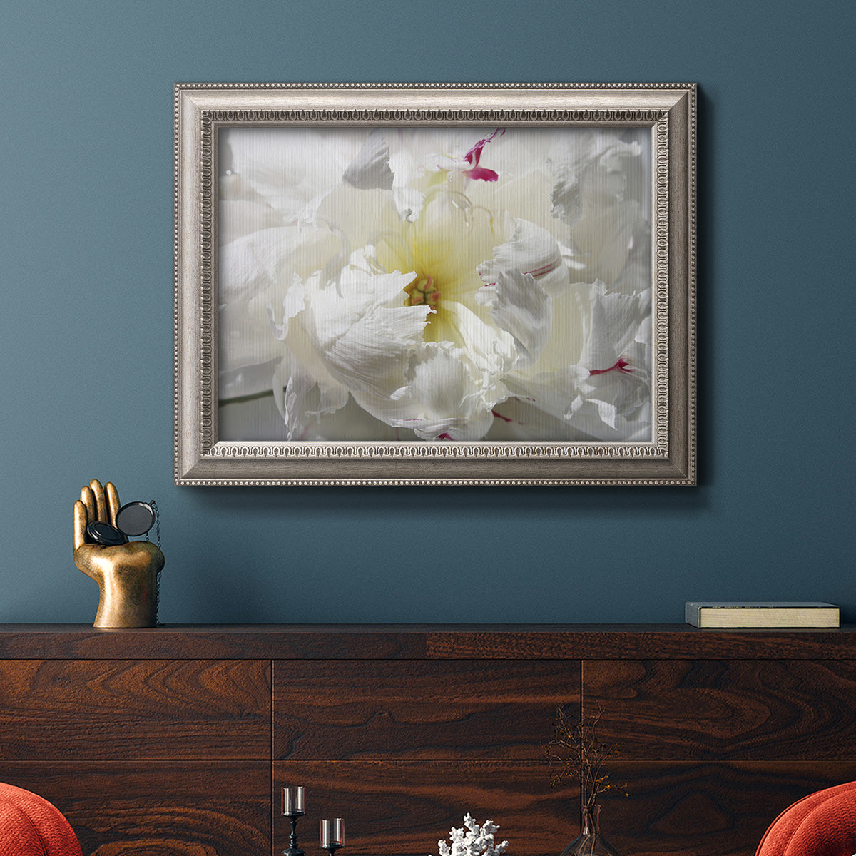 Close up view of peony petals in an ornate vintage silver frame displayed in a dark-toned interior setting.