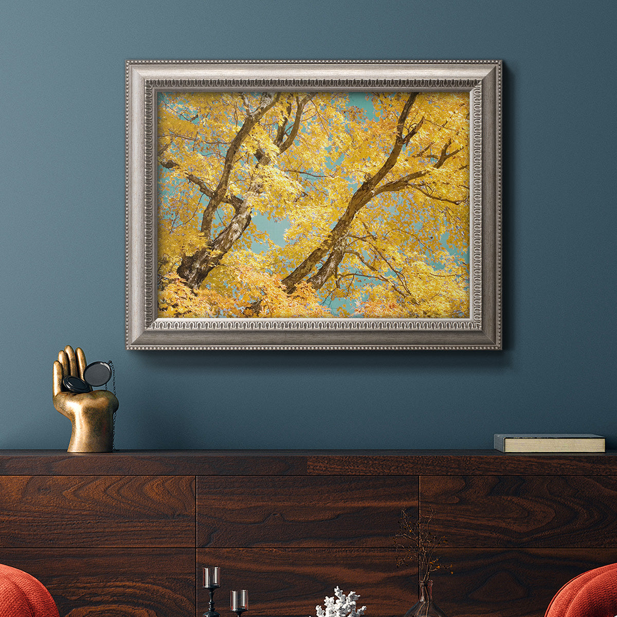Vibrant yellow autumn leaves on branches in an ornate vintage silver frame displayed in a dark-toned interior setting.