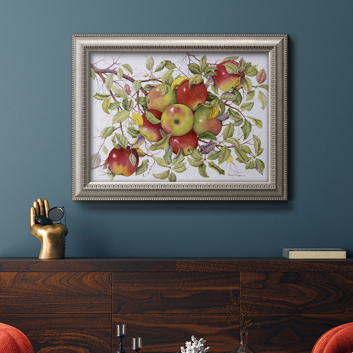 Classic still life painting of apples in an ornate vintage silver frame displayed in a dark-toned interior setting.