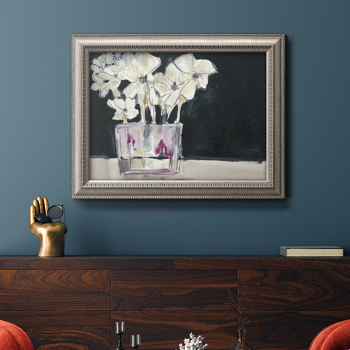 Contemporary floral watercolor with white flowers in an ornate vintage silver frame displayed in a dark-toned interior setting.