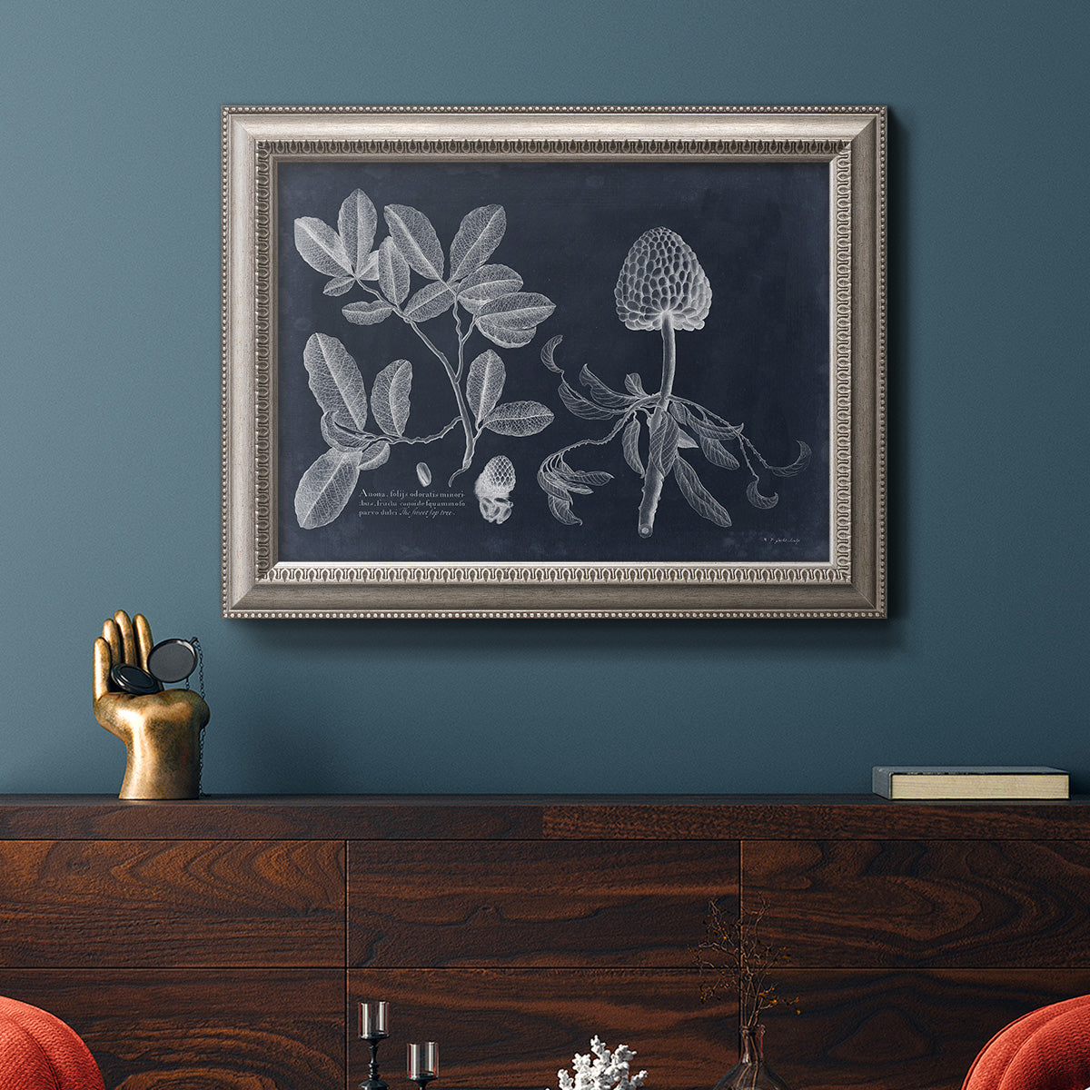 Antique botanical foliage illustration on navy background in an ornate vintage silver frame displayed in a dark-toned interior setting.