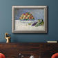 Impressionist still life painting with peaches and grapes in an ornate vintage silver frame displayed in a dark-toned interior setting.