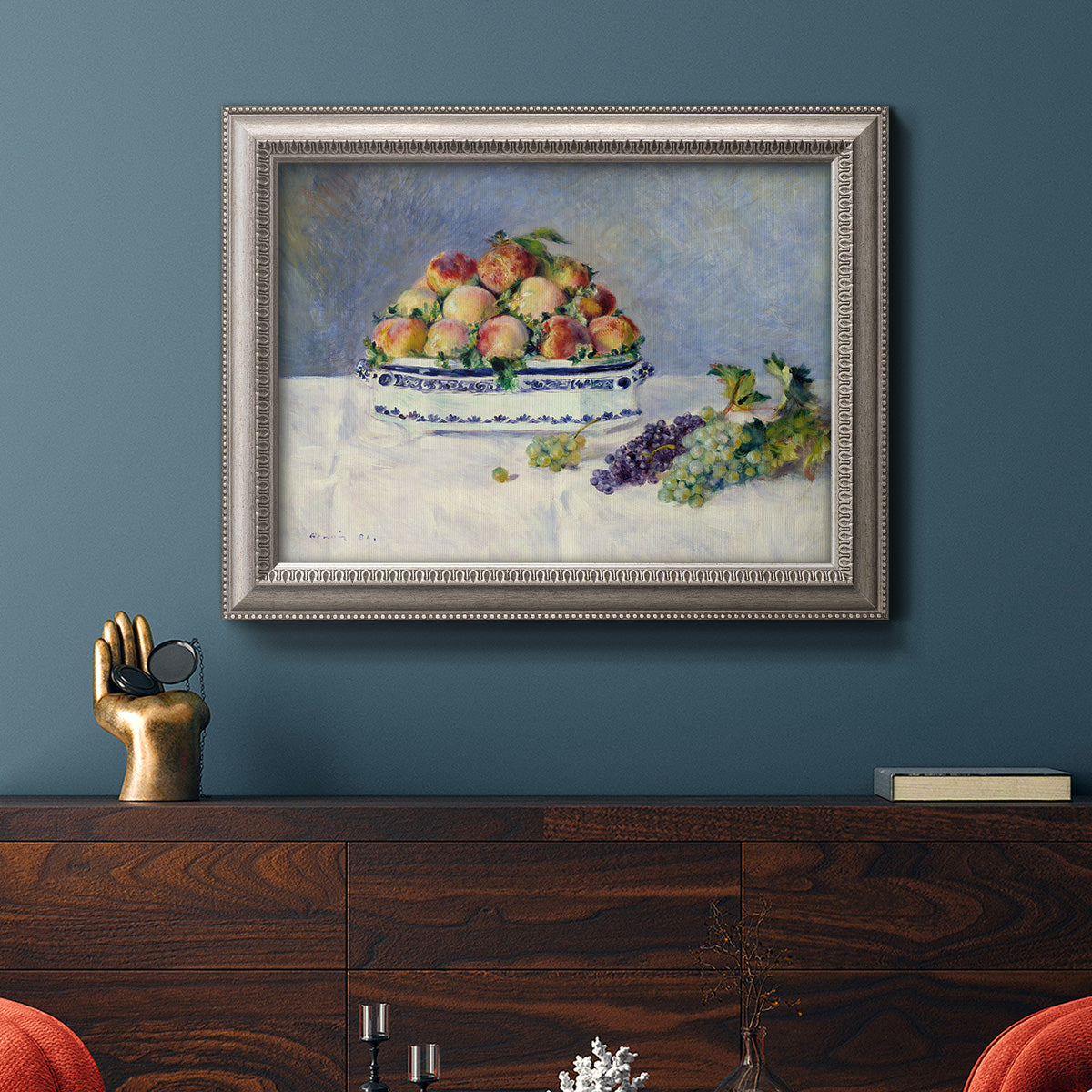 Impressionist still life painting with peaches and grapes in an ornate vintage silver frame displayed in a dark-toned interior setting.