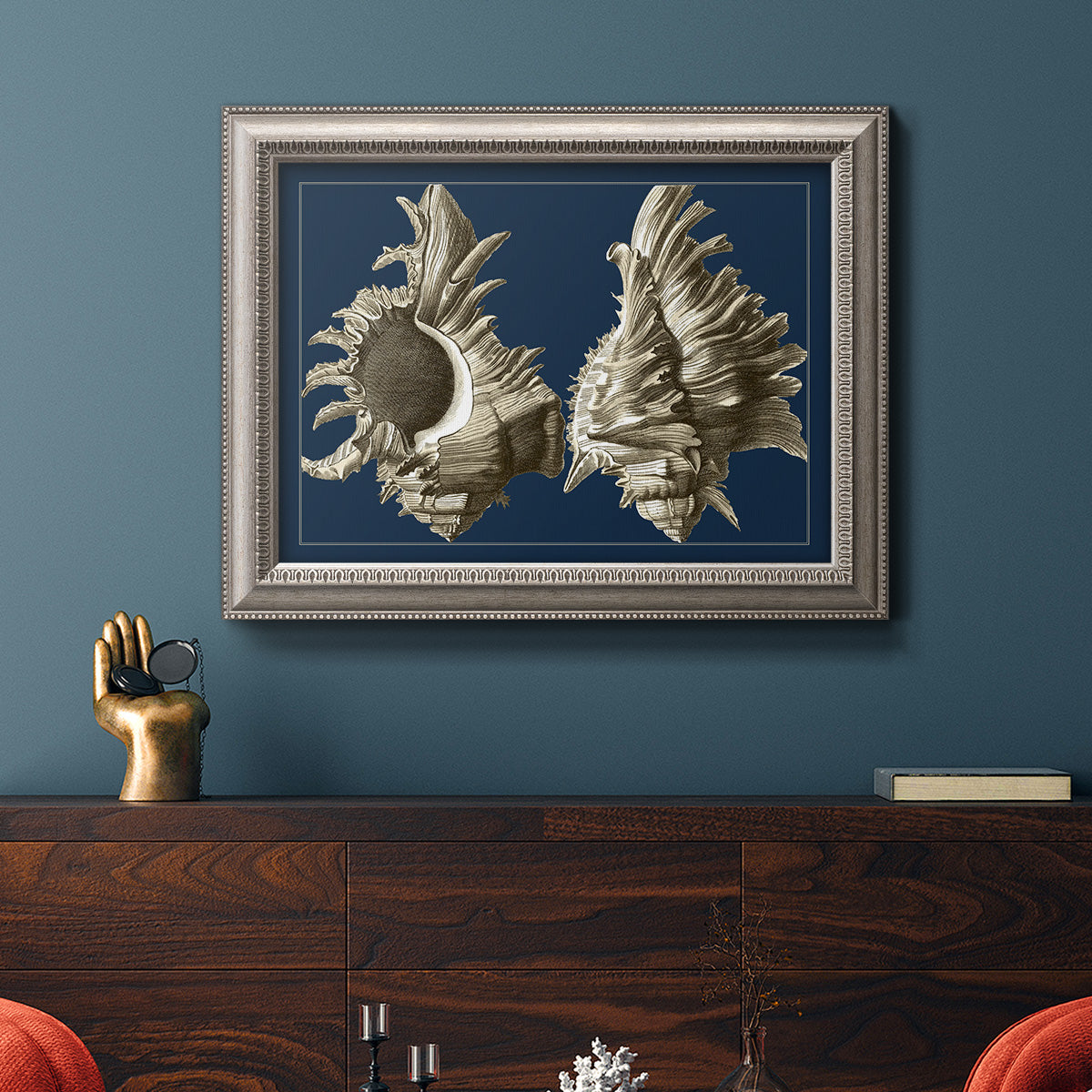 Vintage nautical conch shell artwork on navy background in an ornate vintage silver frame displayed in a dark-toned interior setting.