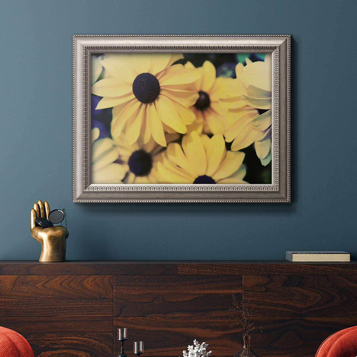Contemporary black-eyed Susan floral photography in an ornate vintage silver frame displayed in a dark-toned interior setting.
