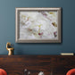 White peonies in bloom in an ornate vintage silver frame displayed in a dark-toned interior setting.