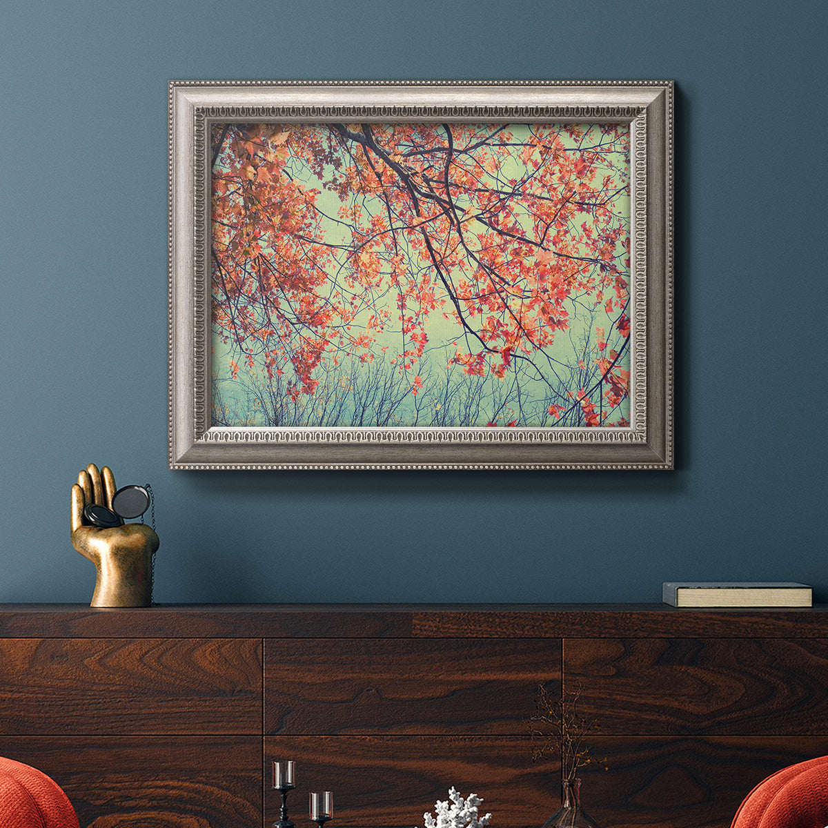 Eclectic fall floral landscape artwork in an ornate vintage silver frame displayed in a dark-toned interior setting.