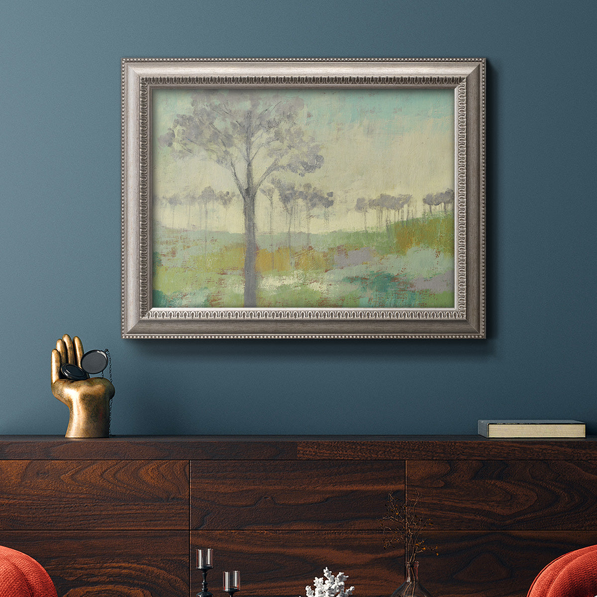 Traditional watercolor tree landscape artwork in an ornate vintage silver frame displayed in a dark-toned interior setting.