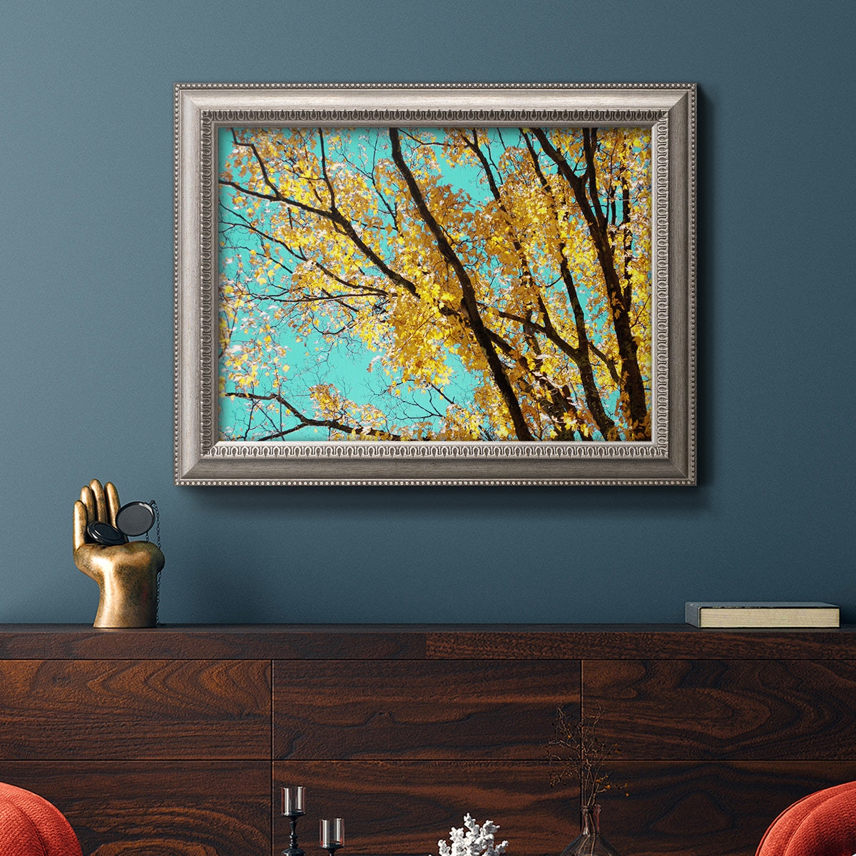 Bright autumn leaves against a blue sky in an ornate vintage silver frame displayed in a dark-toned interior setting.