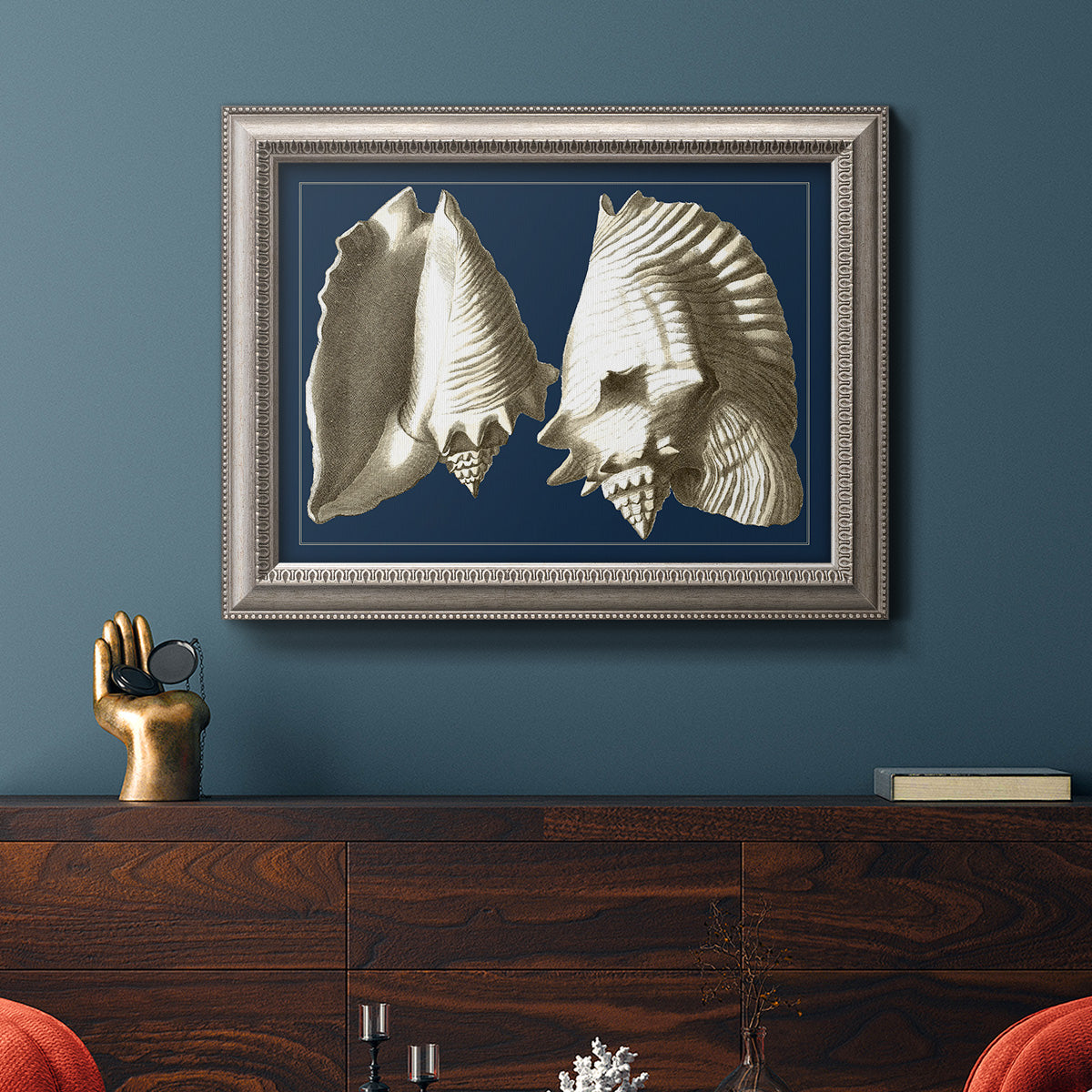 Vintage conch shell illustration on navy background in an ornate vintage silver frame displayed in a dark-toned interior setting.