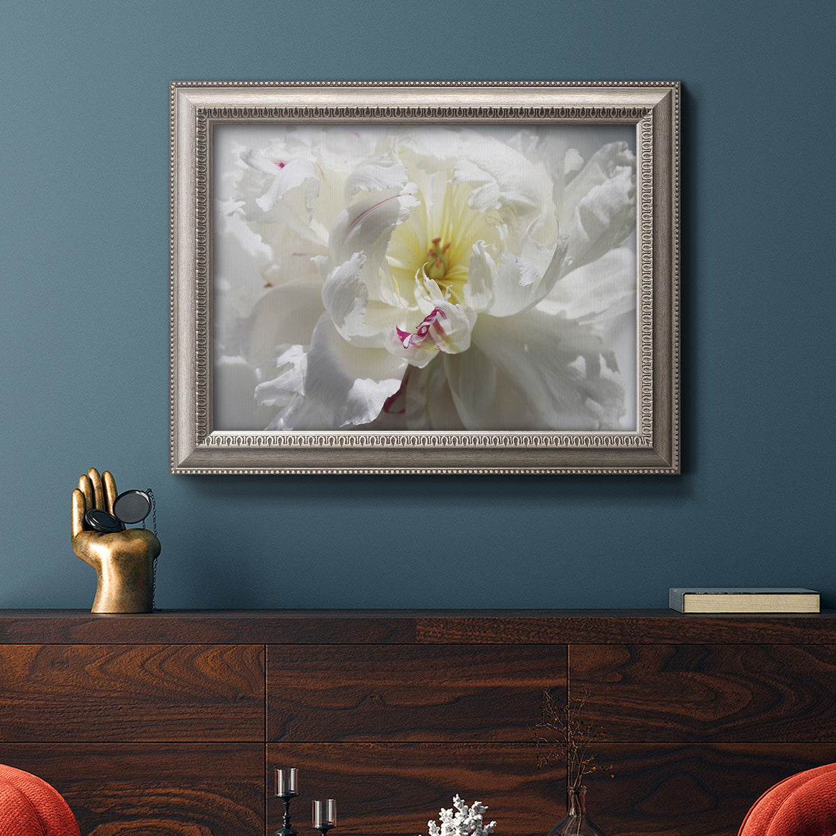 Neutral white peony photography in an ornate vintage silver frame displayed in a dark-toned interior setting.