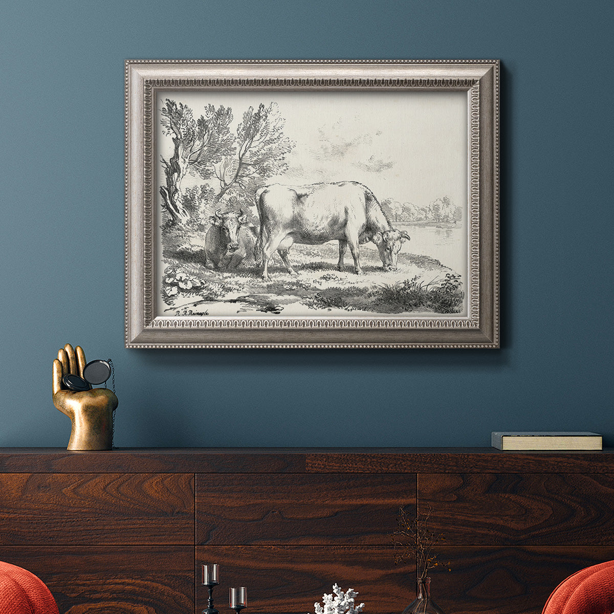 Traditional rural landscape scene by Nicolas Berchem in an ornate vintage silver frame displayed in a dark-toned interior setting.