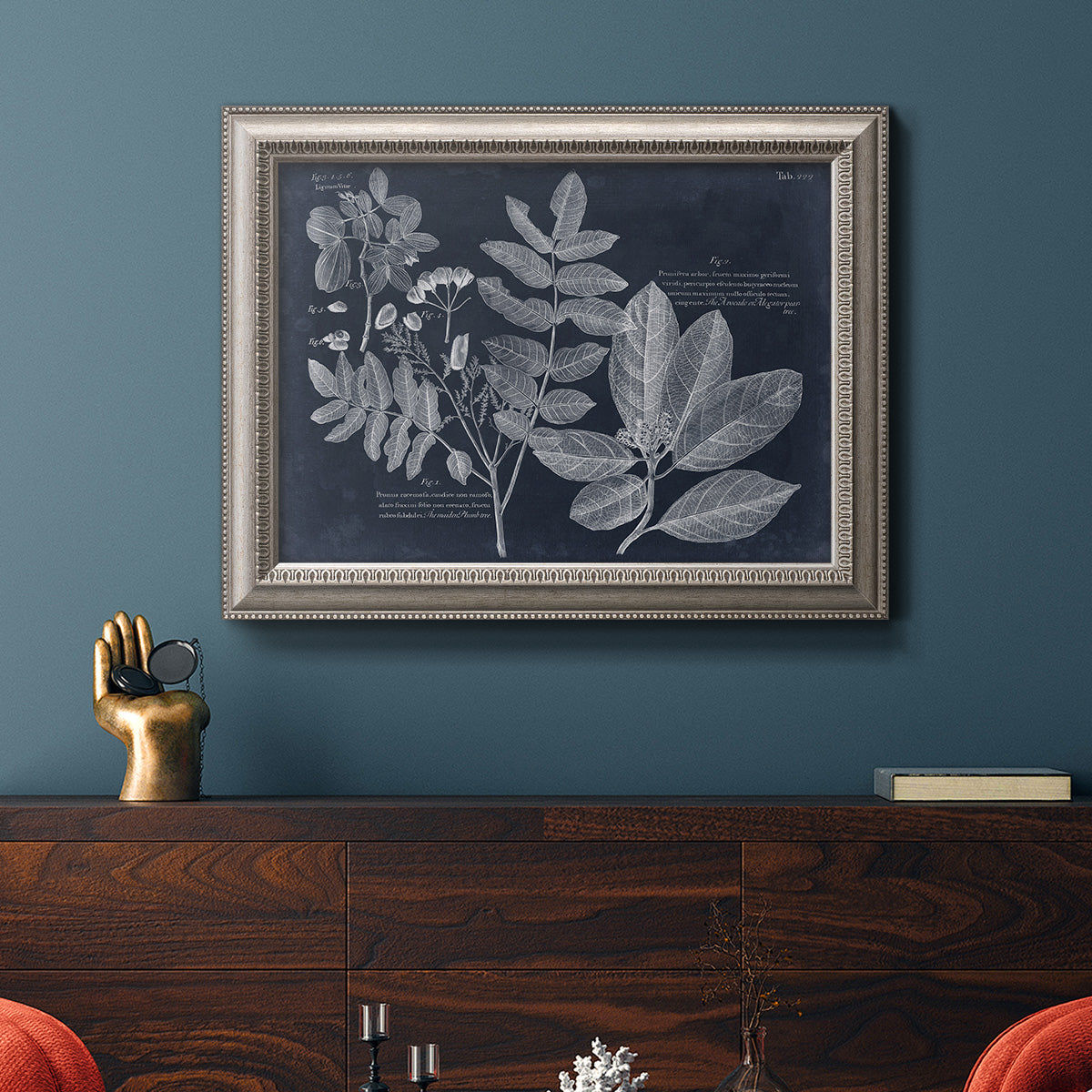 Antique botanical foliage artwork on navy background in an ornate vintage silver frame displayed in a dark-toned interior setting.