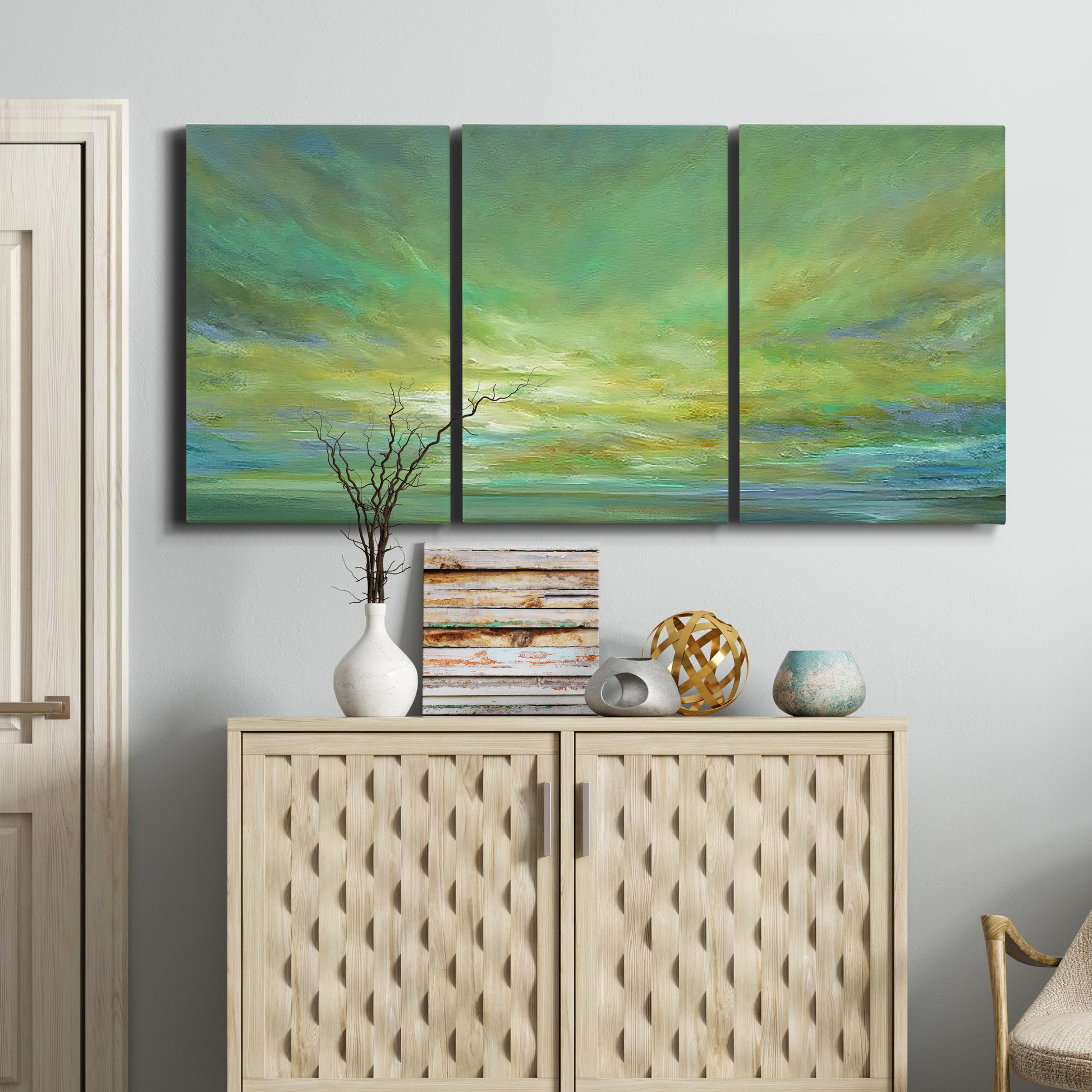 Three-panel canvas wall art featuring coastal shoreline under open sky, displayed above a cabinet in an entryway.