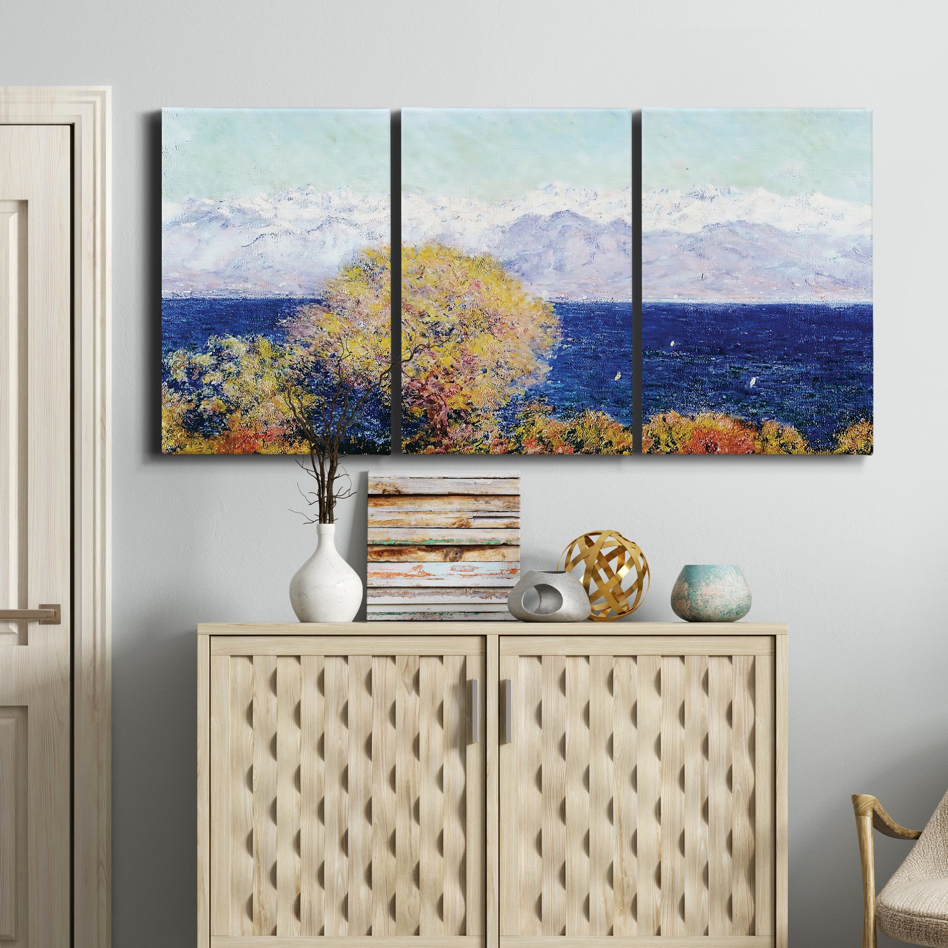 Three-panel canvas wall art featuring mediterranean coastline with headland, displayed above a cabinet in an entryway.