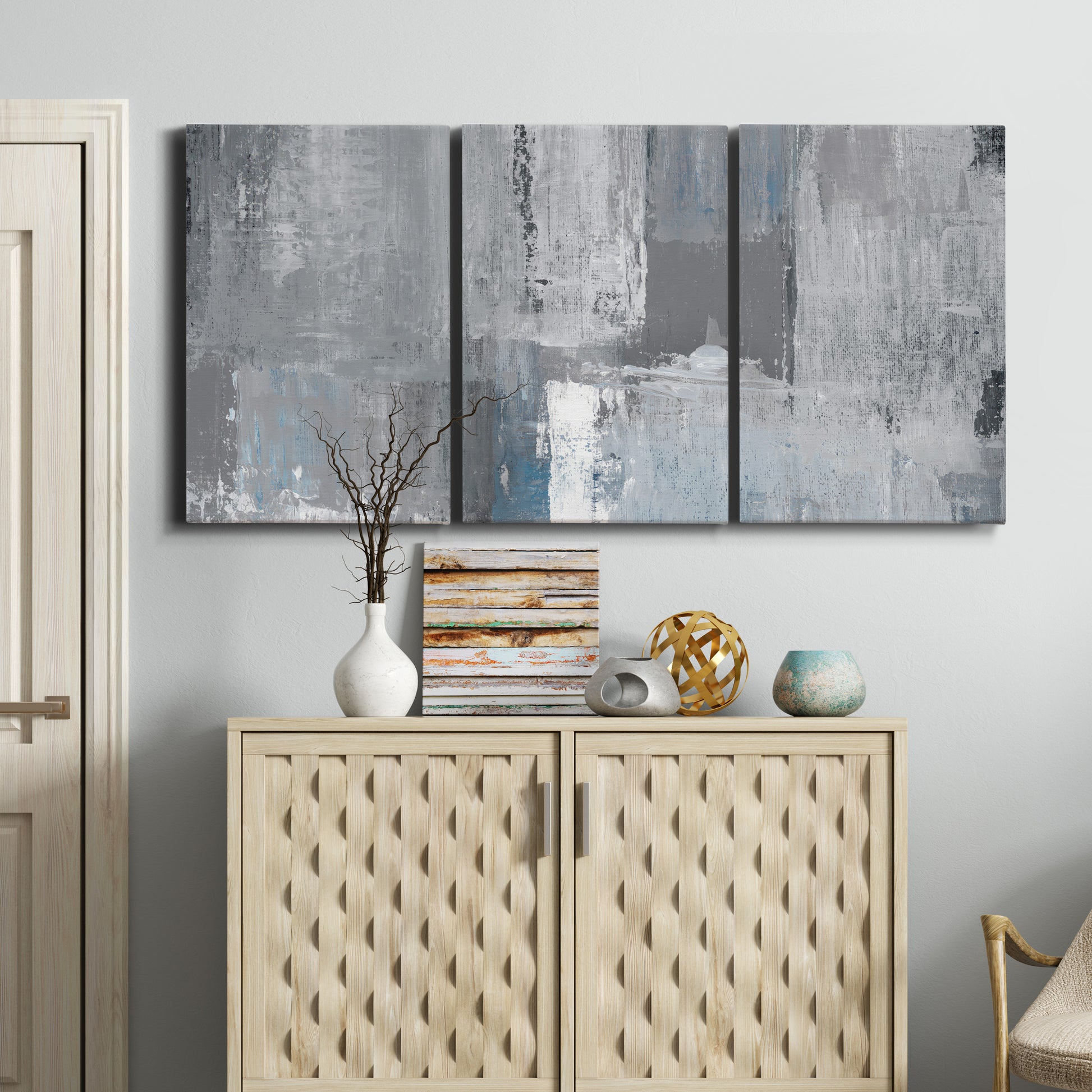 Three-panel canvas wall art featuring cool toned industrial abstract blues, displayed above a cabinet in an entryway.