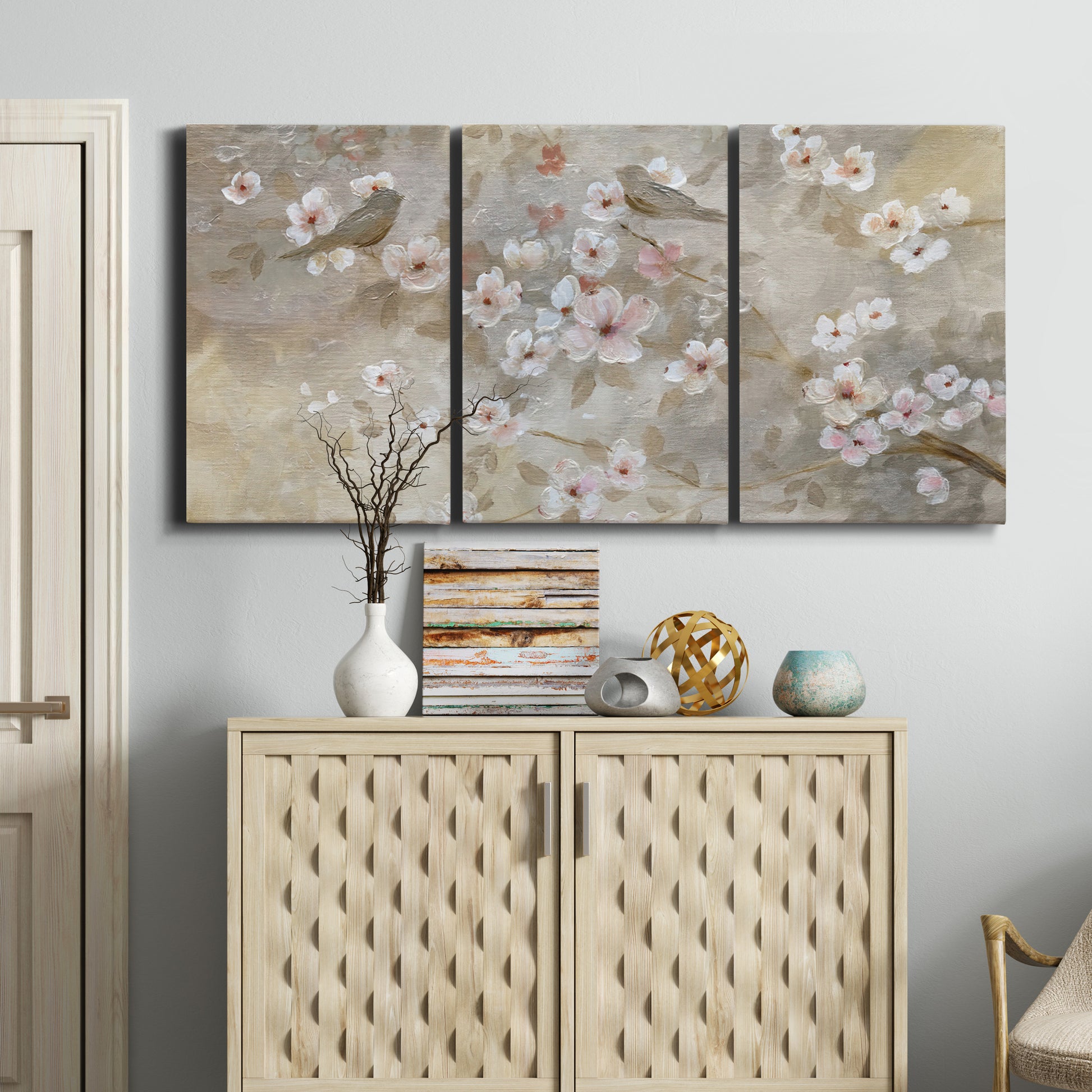 Three-panel canvas wall art featuring early spring blossoms in soft tones, displayed above a cabinet in an entryway.