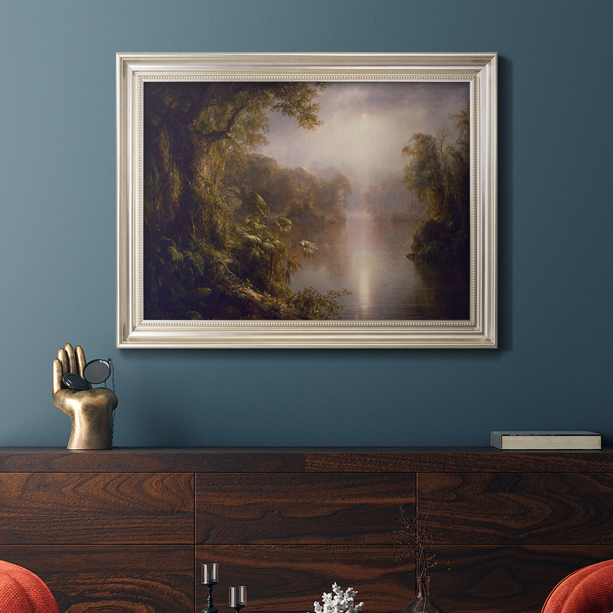 Luminous romantic landscape painting by Frederic Edwin Church in an ornate champagne frame displayed in a dark-toned interior setting.